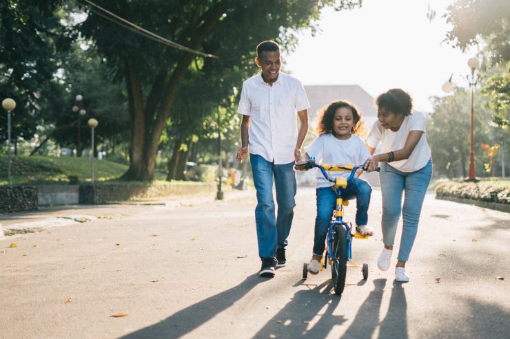 man standing beside his wife teaching their child how to ride bicycle