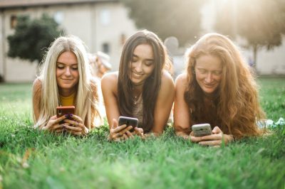 female friends browsing smartphone on lawn