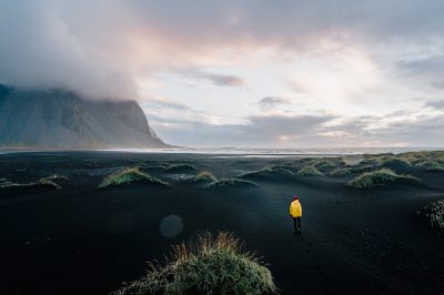 person in yellow jacket standing on green grass field near mountain